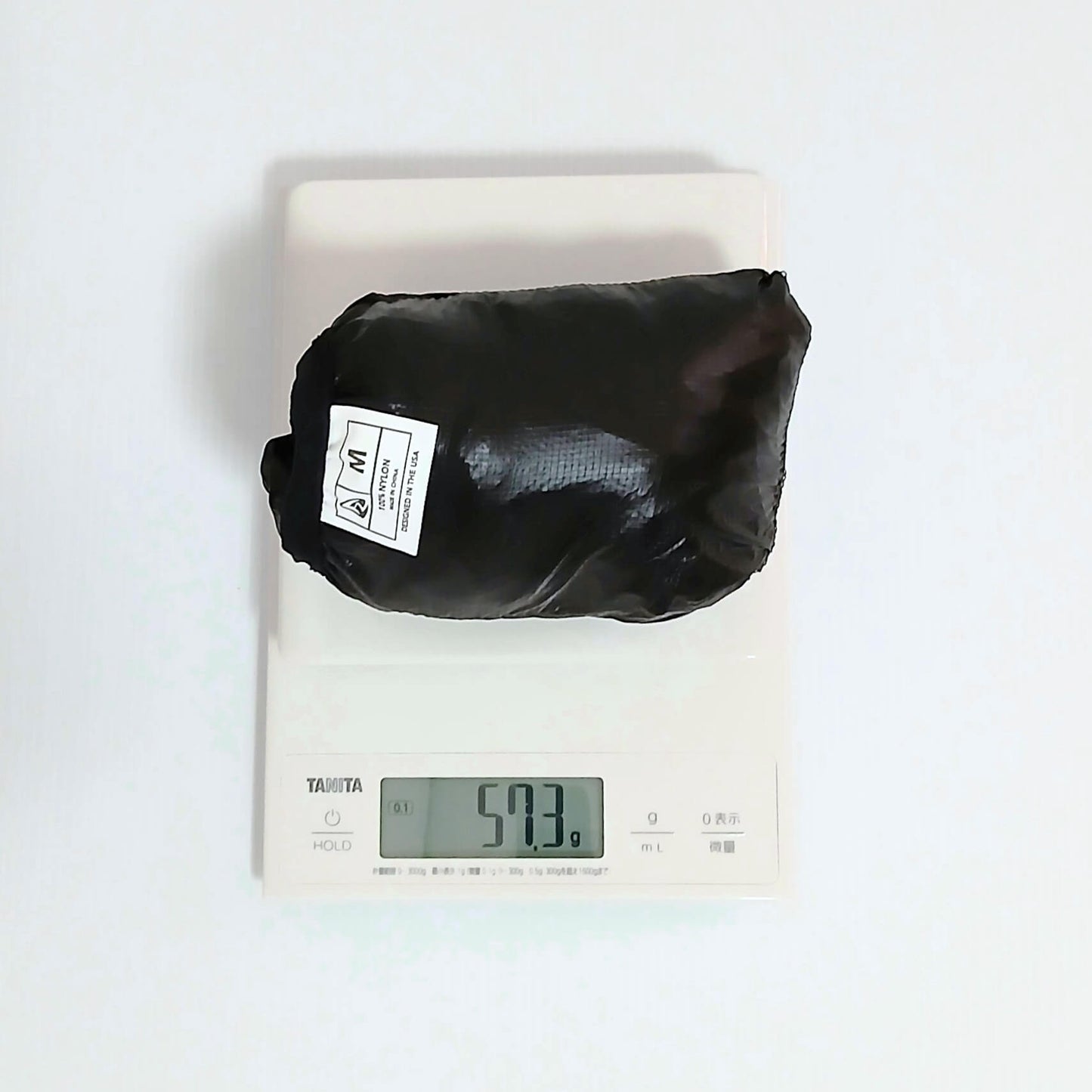 Zpacks Ventum Wind Shell Jacket ベンタムウインドシェルジャケット Black Mサイズを本体一体型ポケットに収納しデジタルスケールで計量、実測57.3gを表示の実物写真 - 山道具とULギアのお店 Ascend Lite