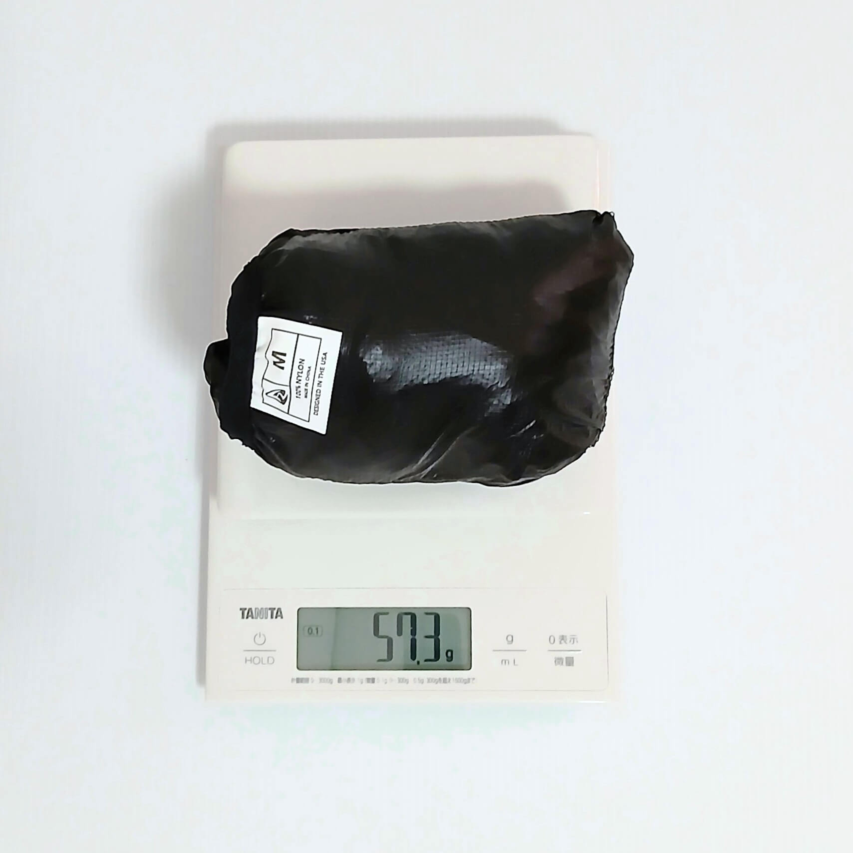 Zpacks Ventum Wind Shell Jacket ベンタムウインドシェルジャケット Black Mサイズを本体一体型ポケットに収納しデジタルスケールで計量、実測57.3gを表示の実物写真 - 山道具とULギアのお店 Ascend Lite