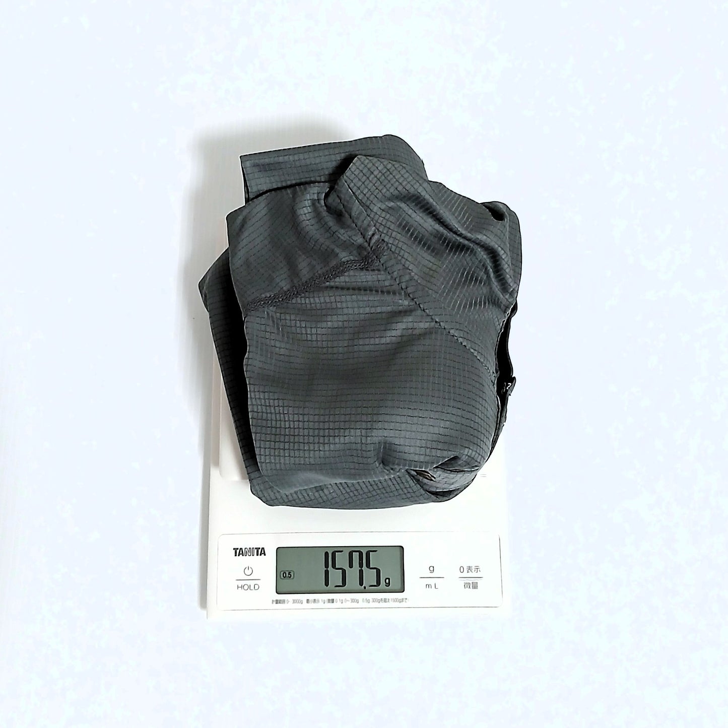 Zpacks Trail Cool Sun Hoody トレイルクールサンフーディ Gray Mサイズを畳んでデジタルスケールで計量、実測157.5gを表示。生地の格子状の織り目も見える実物写真 - 山道具とULギアのお店 Ascend Lite