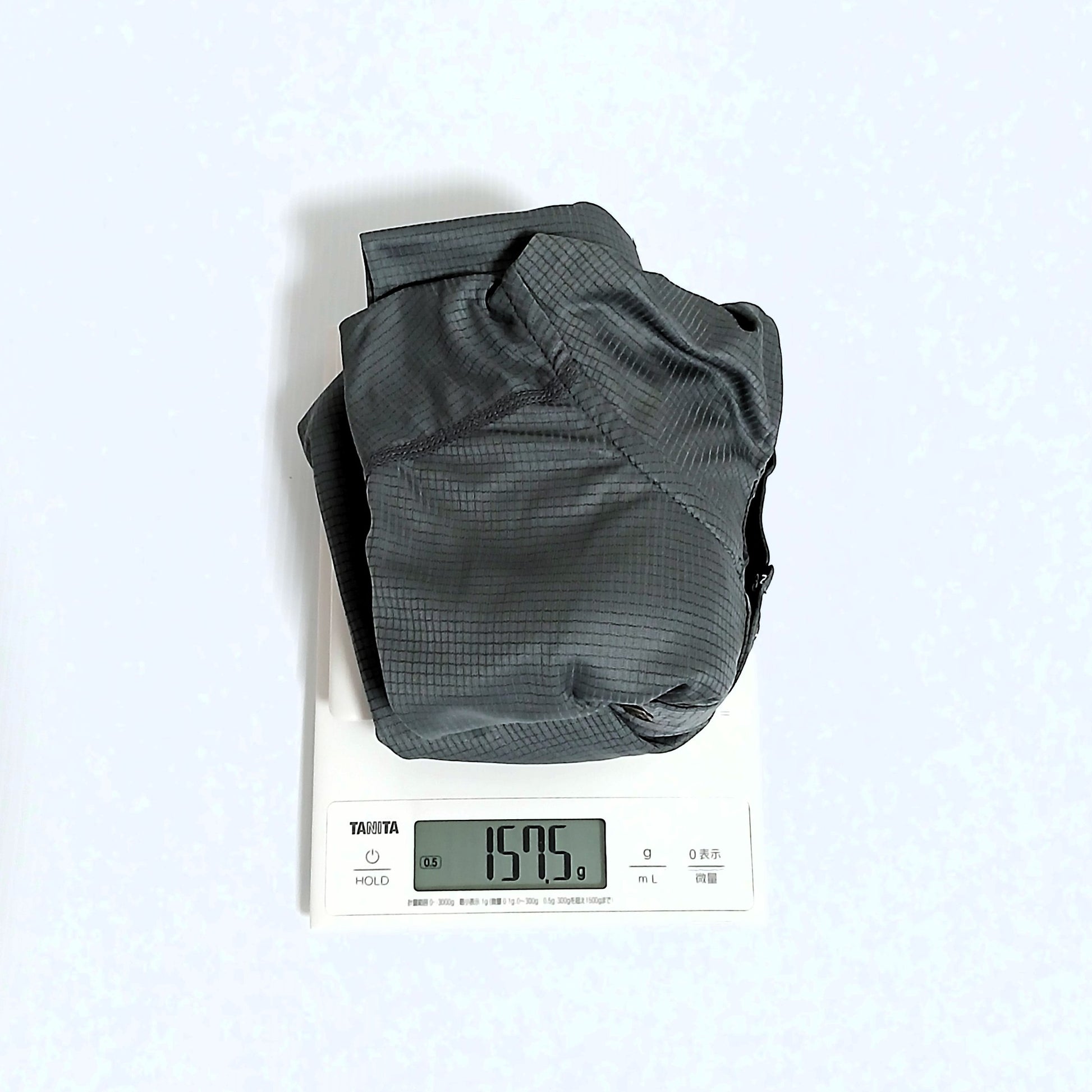 Zpacks Trail Cool Sun Hoody トレイルクールサンフーディ Gray Mサイズを畳んでデジタルスケールで計量、実測157.5gを表示。生地の格子状の織り目も見える実物写真 - 山道具とULギアのお店 Ascend Lite