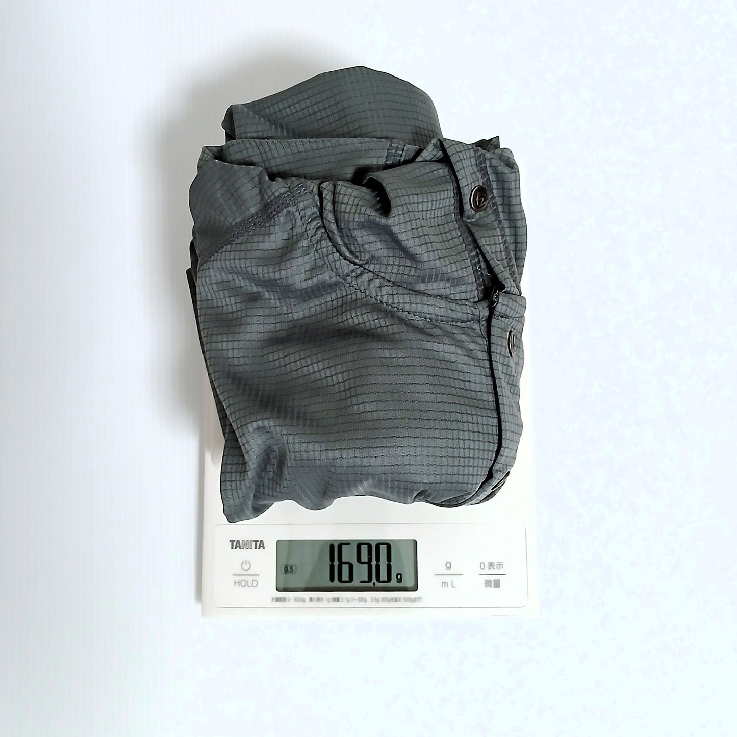 Zpacks Trail Cool Sun Hoody トレイルクールサンフーディ Gray Lサイズを畳んでデジタルスケールで計量、実測169.0gを表示。胸元のスナップボタンが視認できる実物写真 - 山道具とULギアのお店 Ascend Lite