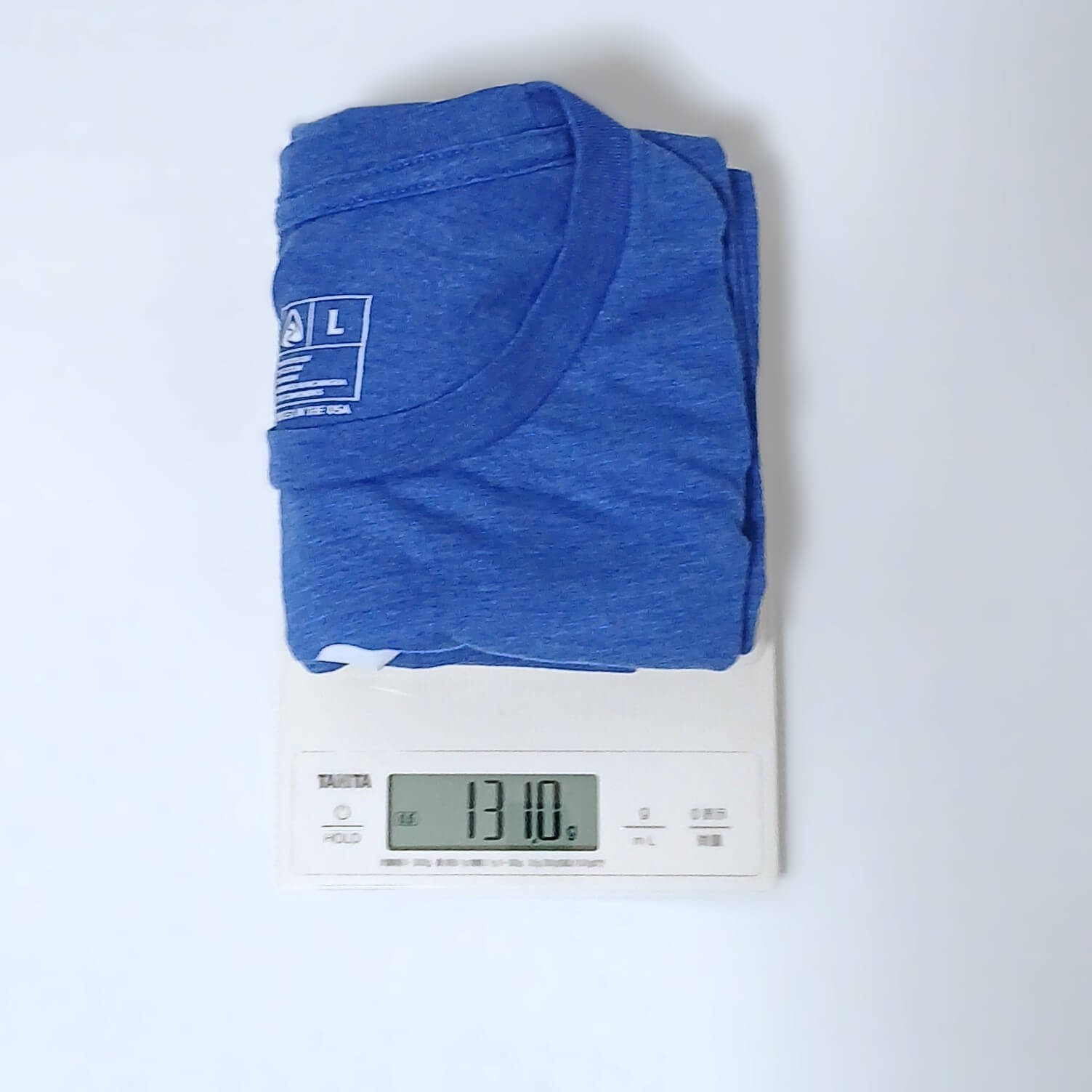 Zpacks Crest T-Shirt クレストTシャツ ブルーのLサイズを畳んでデジタルスケールにのせ、131.0gを表示した計量の実物写真。首元にLサイズのタグ - 山道具とULギアのお店 Ascend Lite