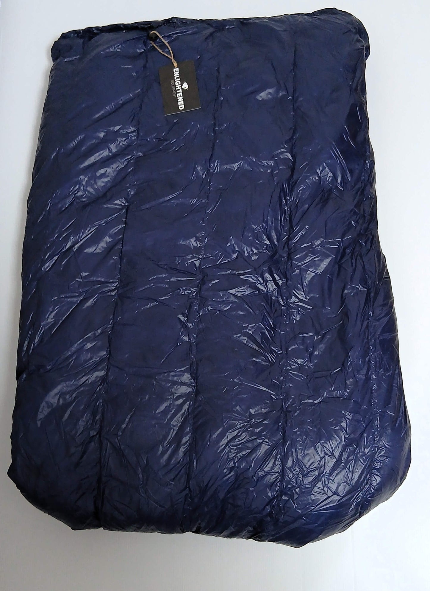 Enlightened Equipment Revelation Sleeping Quilt 50°F Navy 10D 本体を畳んだ全体・光沢のある10Dナイロン生地とブランドタグ付きの実物写真 - 山道具とULギアのお店 Ascend Lite