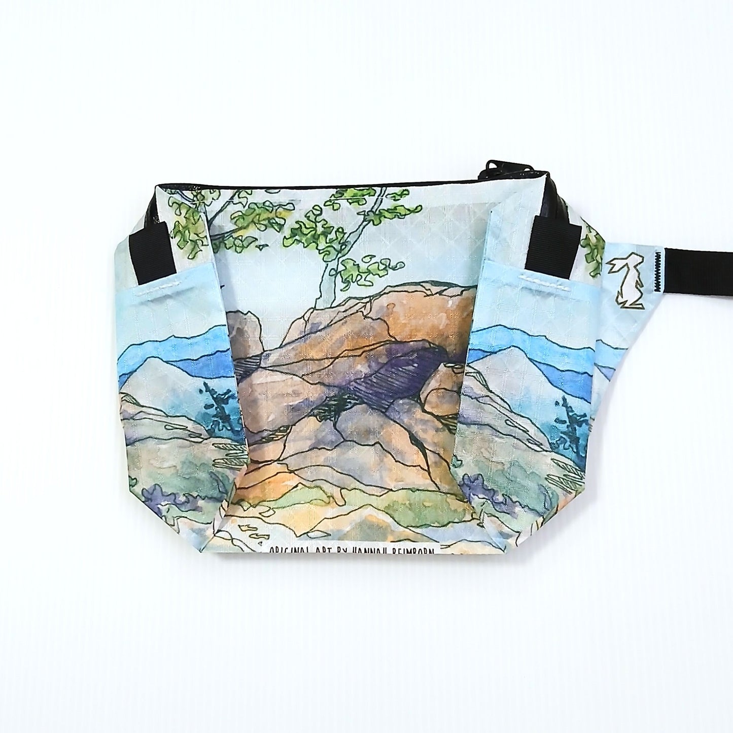 High Tail Designs The Ultralight Fanny Pack ファニーパック Lost Gulch Lookout（Hannah Beimborn） 水色の空と青い遠山を背に茶色の大岩が横たわる展望地を水彩線画で描いた柄の正面全体と、上部から垂れる緑の枝葉の実物写真 - 山道具とULギアのお店 Ascend Lite