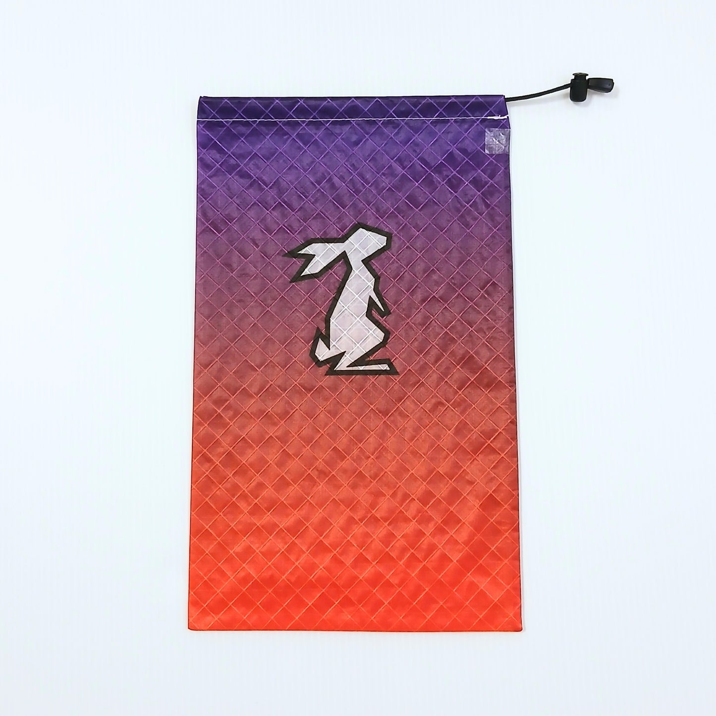 High Tail Designs Ultralight Drawstring Stuff Sack ドローストリングスタッフサック Sunset 濃紫の空からオレンジ・朱赤へ暮れていくグラデーション柄、中央にクリーム色のウサギ輪郭ロゴ、生地の45度クロス格子が光る実物写真 - 山道具とULギアのお店 Ascend Lite