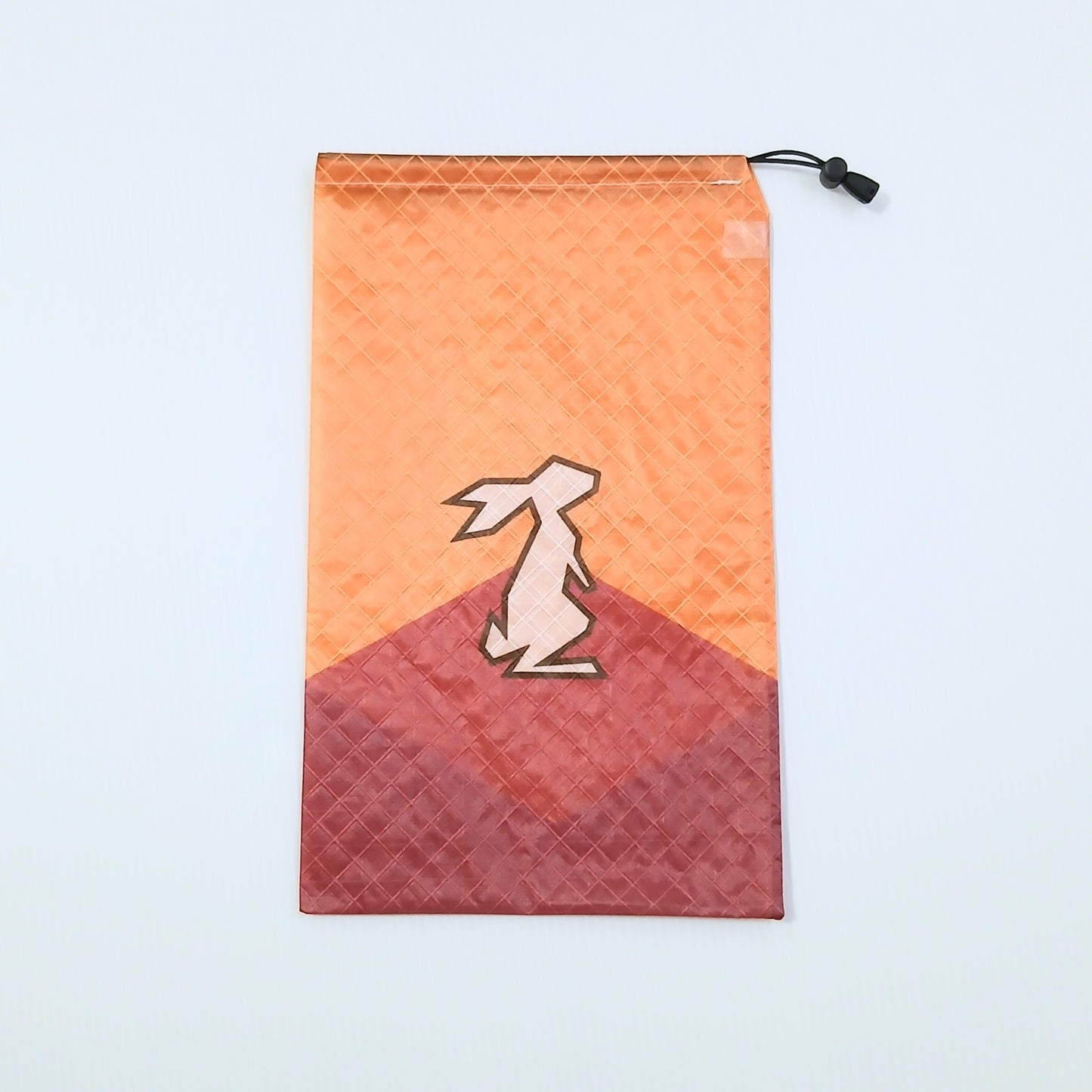 High Tail Designs Ultralight Drawstring Stuff Sack ドローストリングスタッフサック Blaze Sunlight オレンジの空と赤茶の山を組み合わせた山型カラーブロック柄、中央にクリーム色のウサギのシルエットの実物写真 - 山道具とULギアのお店 Ascend Lite