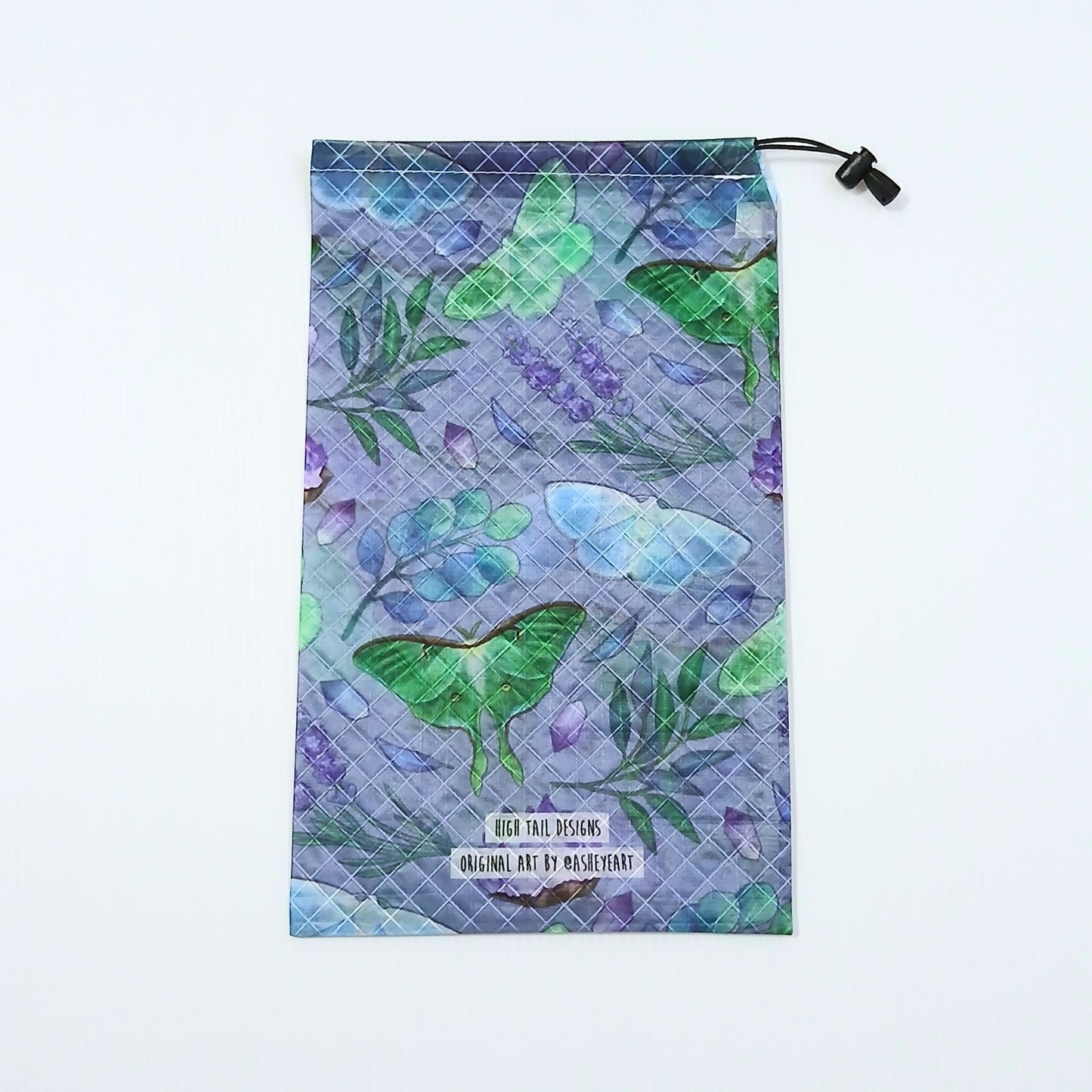 High Tail Designs Ultralight Drawstring Stuff Sack ドローストリングスタッフサック Nocturna 藤色の地に緑と水色の大型の蛾、紫の花とアメジスト状の結晶を散らした総柄、裾にブランド名とアーティストクレジットの2行印字の実物写真 - 山道具とULギアのお店 Ascend Lite