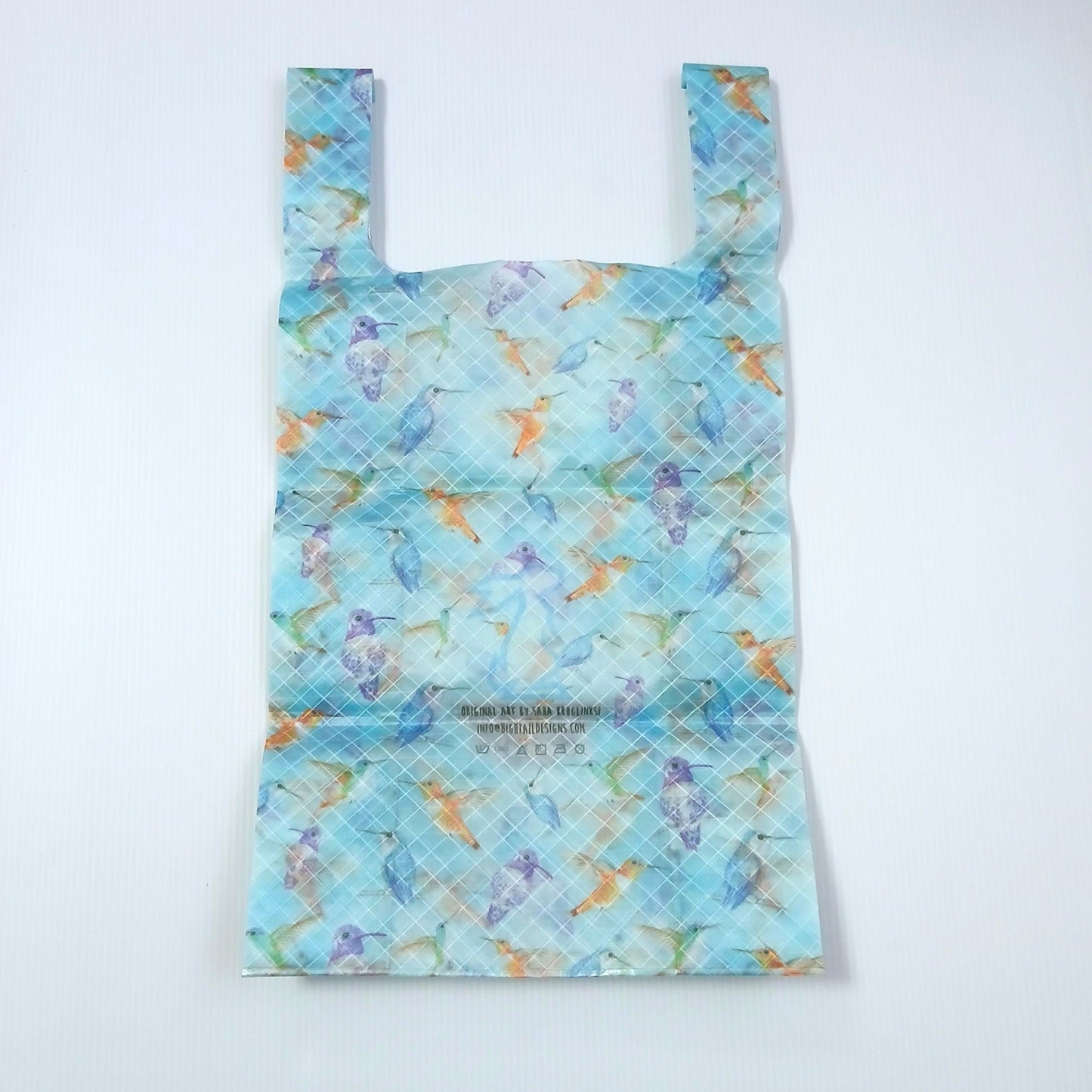 High Tail Designs TX Small Shopping Bag ショッピングバッグ S Hummingbirds 水色の地に青・紫・オレンジのハチドリが舞う水彩柄で、斜め45°のクロスプライ格子が全面に浮かぶ。中央にアーティストクレジット印字と洗濯表示アイコン、幅広ハンドルの平置き正面全体の実物写真 - 山道具とULギアのお店 Ascend Lite