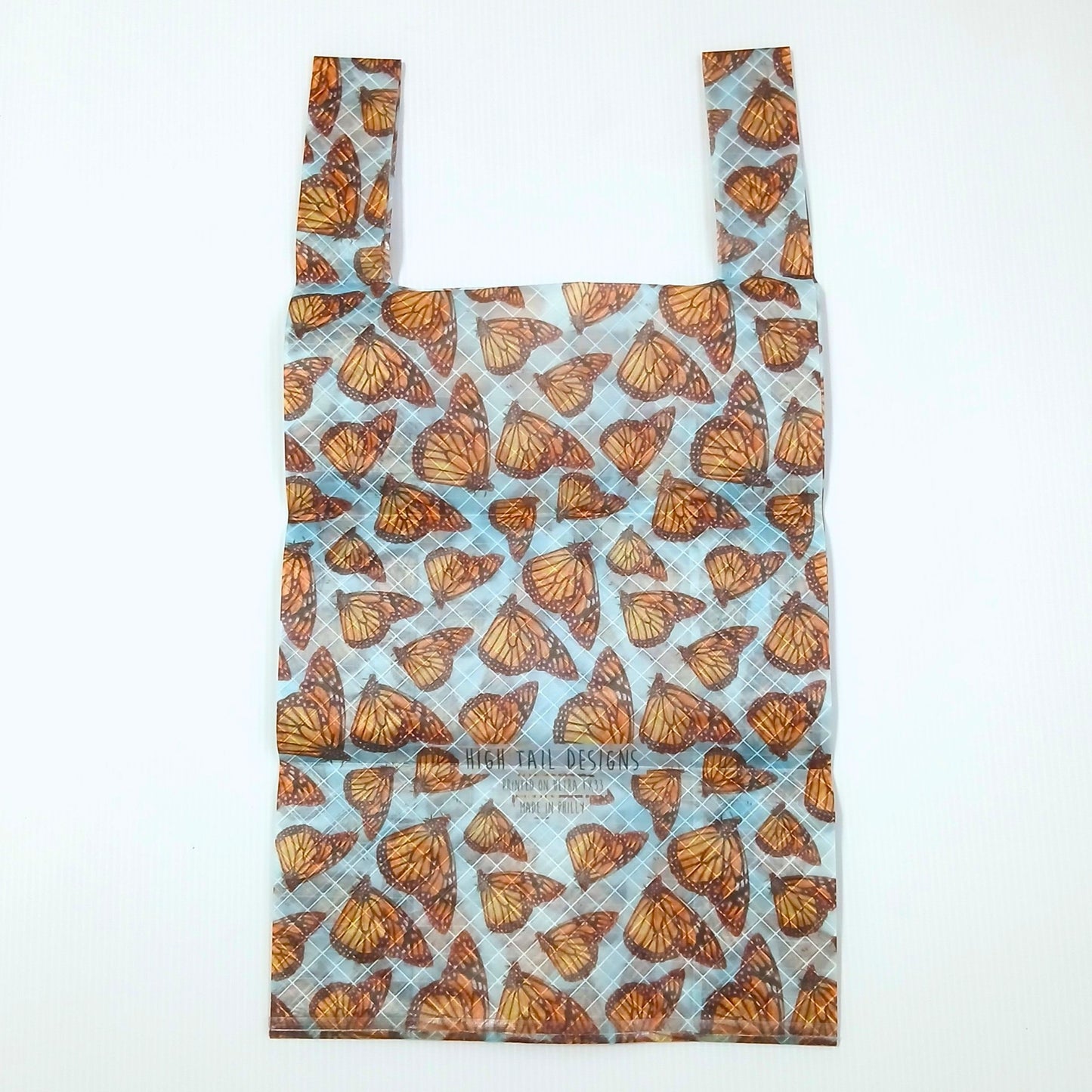 High Tail Designs TX Small Shopping Bag ショッピングバッグ S Monarchs 淡い水色の地にオレンジと黒のオオカバマダラの翅を一面に敷き詰めた柄。中央にブランド名の文字ロゴとアーティストクレジット印字、横一文字の折り目が残る幅広ハンドルの平置き正面全体の実物写真 - 山道具とULギアのお店 Ascend Lite