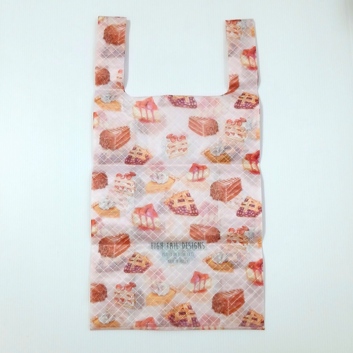 High Tail Designs TX Small Shopping Bag ショッピングバッグ S Cakes & Pies 淡いピンクの地にショートケーキやパイ、タルトの水彩イラストが散る柄。中央にブランド名の文字ロゴとアーティストクレジット印字、横一文字の折り目が残る幅広ハンドルの平置き正面全体の実物写真 - 山道具とULギアのお店 Ascend Lite
