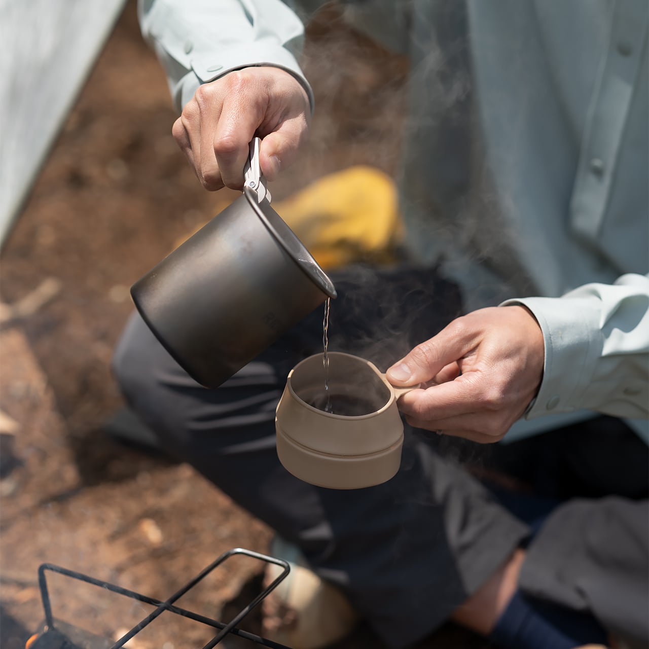 RIDGE MOUNTAIN GEAR Titanium Mug 450ml チタンマグ450ml リフターで挟んで折りたたみカップにお湯を注ぐ様子（公式画像） - 山道具とULギアのお店 Ascend Lite