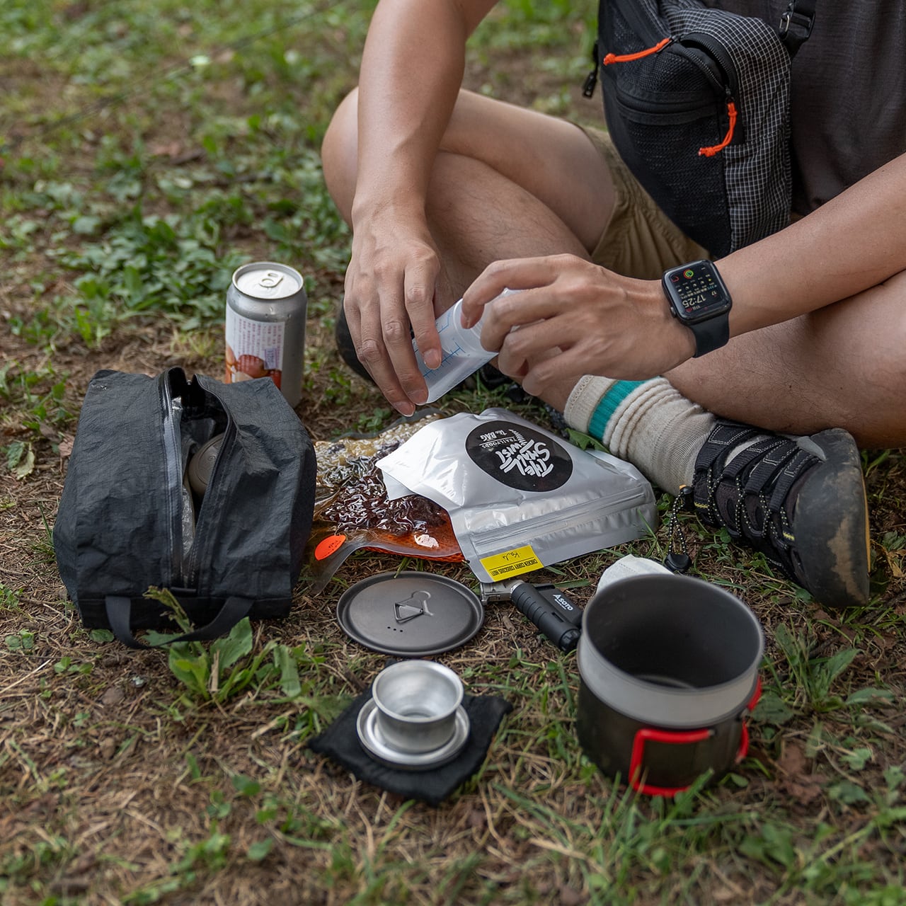 RIDGE MOUNTAIN GEAR JUN OSON×RIDGE Case M ケースM 草地に座り調理道具を取り出して食事を準備する使用シーン（無地モデル・公式画像） - 山道具とULギアのお店 Ascend Lite