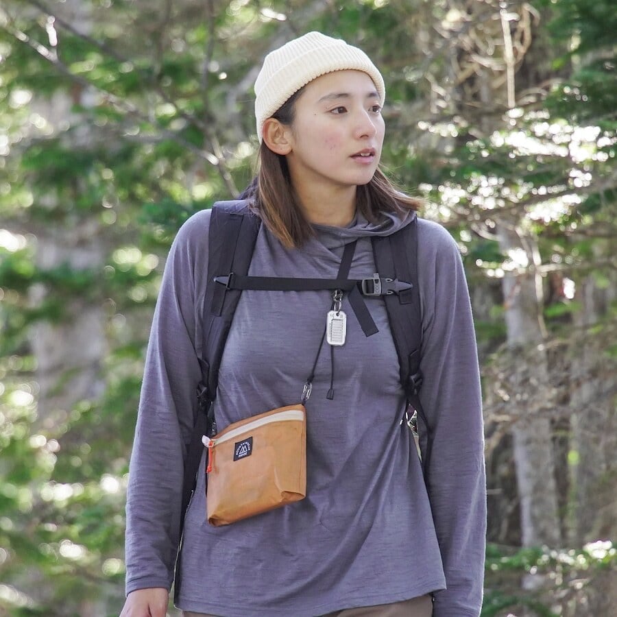 RIDGE MOUNTAIN GEAR Travel Pouch Plus トラベルポーチプラス オレンジ系カラーを肩から斜めがけしたサコッシュ使用シーン（樹林帯）（公式画像） - 山道具とULギアのお店 Ascend Lite