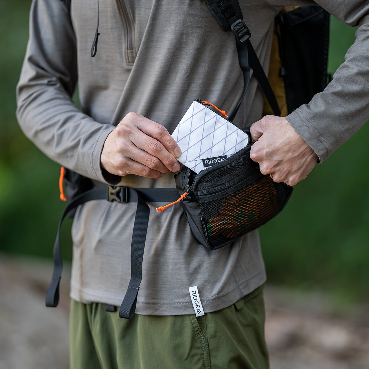 RIDGE MOUNTAIN GEAR Side Increase サイドインクリース ウエストベルトに装着したポーチへ小物入れを出し入れする腰まわりのクローズアップ（公式画像） - 山道具とULギアのお店 Ascend Lite