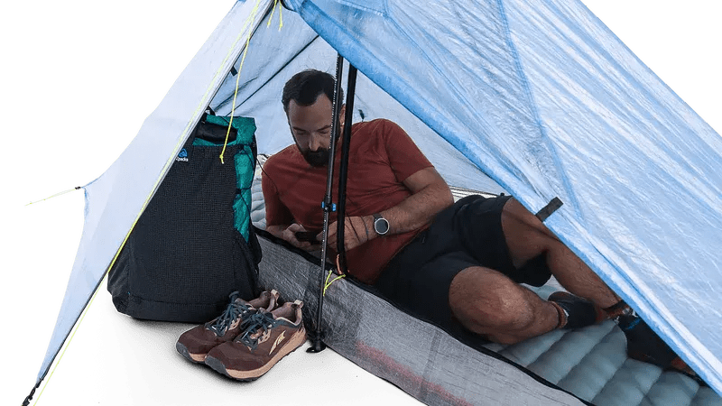 Zpacks Plex Solo Pro Tent プレックスソロプロテント Blue 前室の使用シーン - 片側のストームドアを開けた前室にバックパックとトレイルシューズを置き、室内ではマットに横になって過ごす様子（公式画像） - 山道具とULギアのお店 Ascend Lite