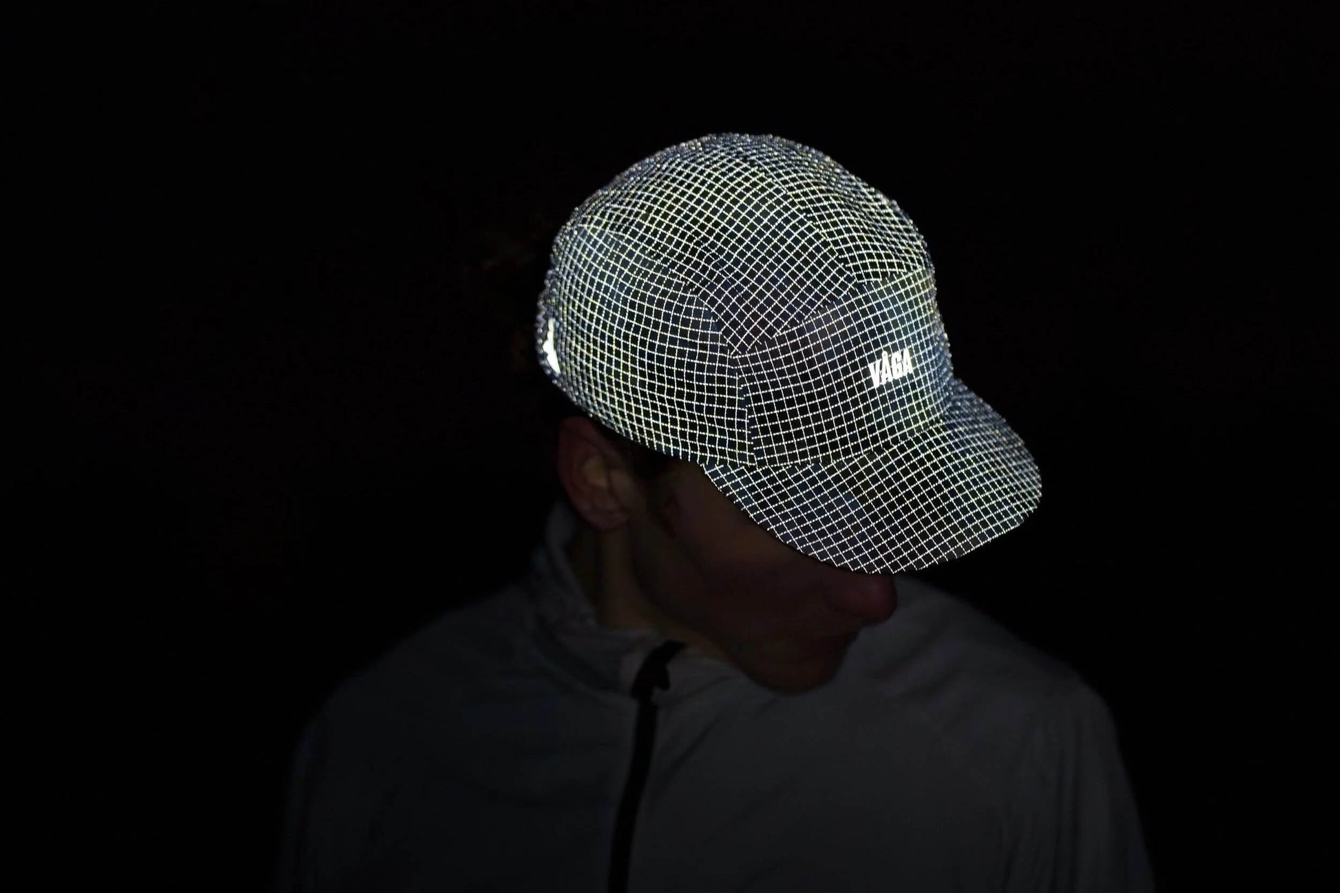 VAGA Night Club Cap ナイトクラブキャップ 暗所での反射の見え方（公式画像） - 光を受けてキャップ全面の格子状リフレクティブが白く浮かび上がる夜間の着用シーン - 山道具とULギアのお店 Ascend Lite